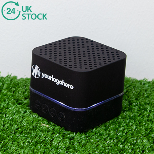 Black LED speaker printed speaker with 'your logo here' branded on. LED light illuminated around the speaker. Sitting on a grass background with an icon that says 24 hours UK stock.